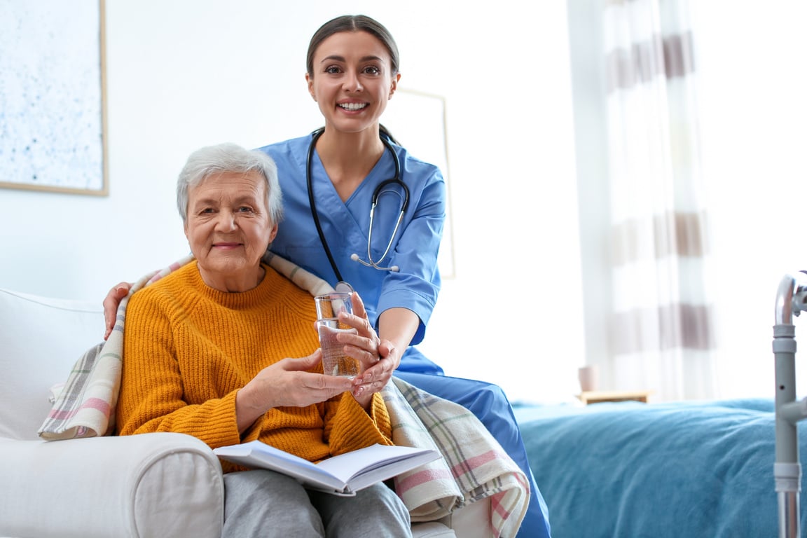 Care Worker Giving Water to Elderly Woman in Geriatric Hospice